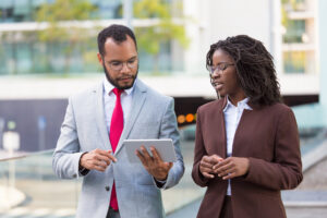 Multiethnic business team watching presentation on tablet on their way to office. Business man showing tablet screen to black female colleague while walking outdoors. Wi-Fi connection concept