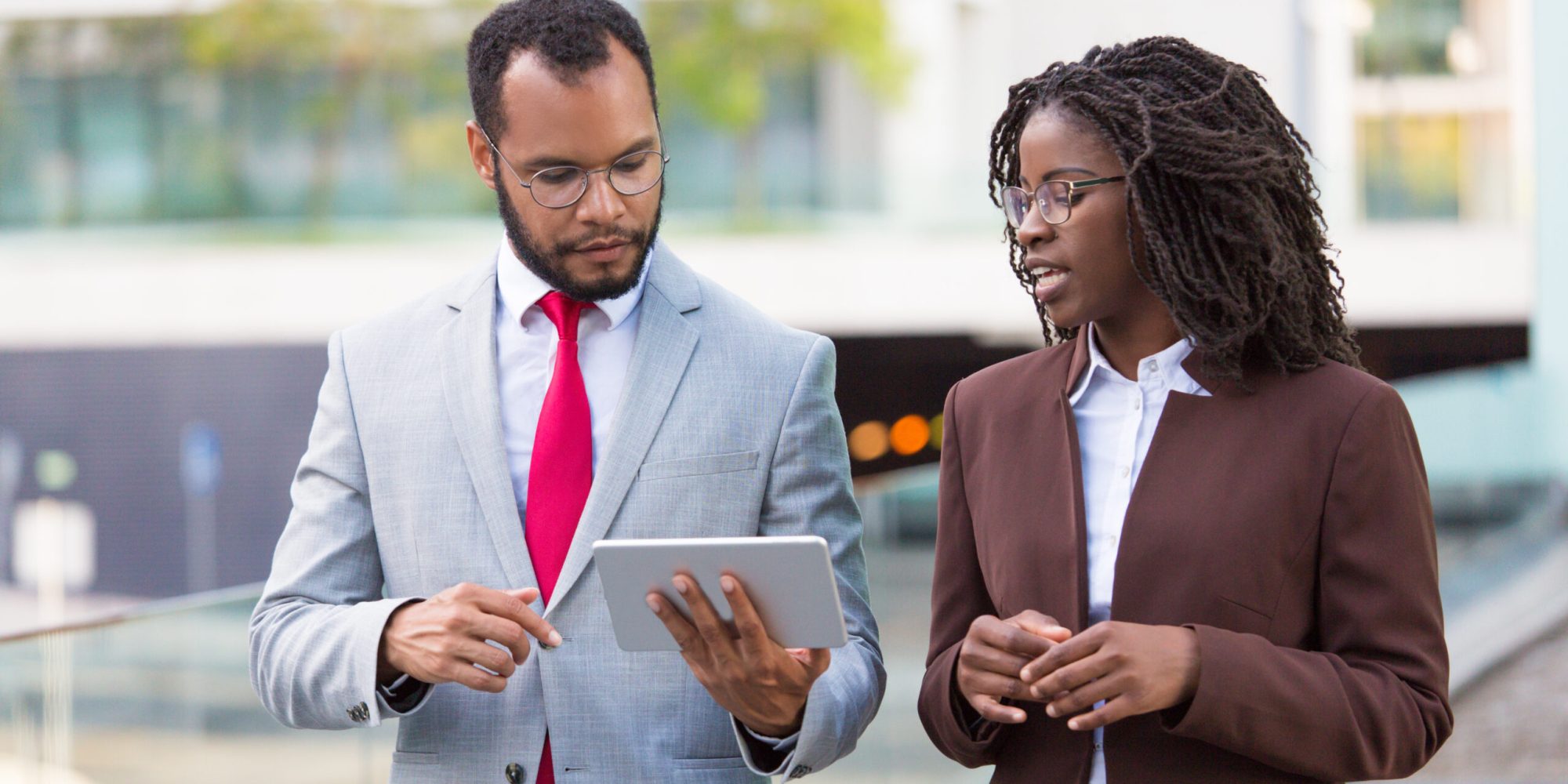 Multiethnic business team watching presentation on tablet on their way to office. Business man showing tablet screen to black female colleague while walking outdoors. Wi-Fi connection concept